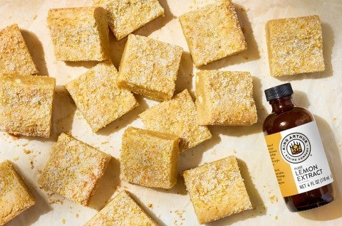 Alex Roberts Lemon Citrus Blondies on parchment paper atop a counter with a bottle of pure citrus extract. - select to zoom