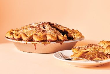An apple pie in a pie tin and a slice on a plate.
