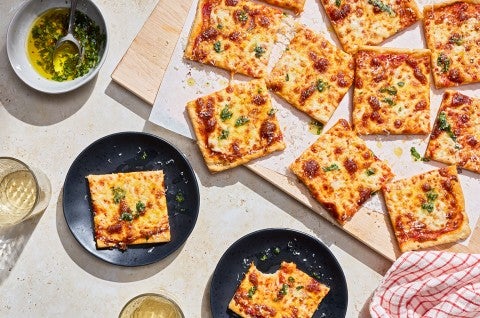 Slices of Gluten-Free Sheet Pan Pizza seen from above and randomly arranged on a cutting board with other slices on plates. - select to zoom