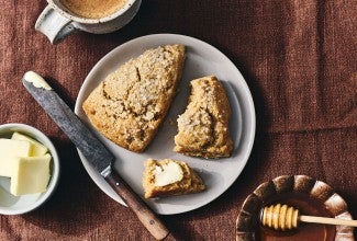 Two Golden Wheat Scones on a plate, one unbroken, the other broken with a dollop of butter on it.
