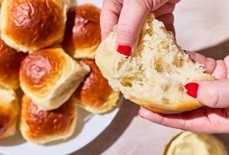 Two hands photographed pulling apart a fluffy homemade dinner roll exposing the airy and moist interior.
