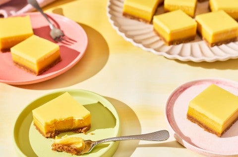 A table set with pastel colored tableware and plates with Passionfruit Bars spread out. - select to zoom