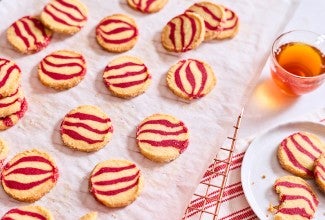 Striped peppermint shortbread cookies laid out on a table with a beverage and plate full of cookies.
